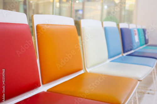 Selective focus shot with copy space of many colorful chairs in a row in the lobby or waiting room in hospital shows joyful, comfortable, clean, bright and happy atmosphere for seated people.