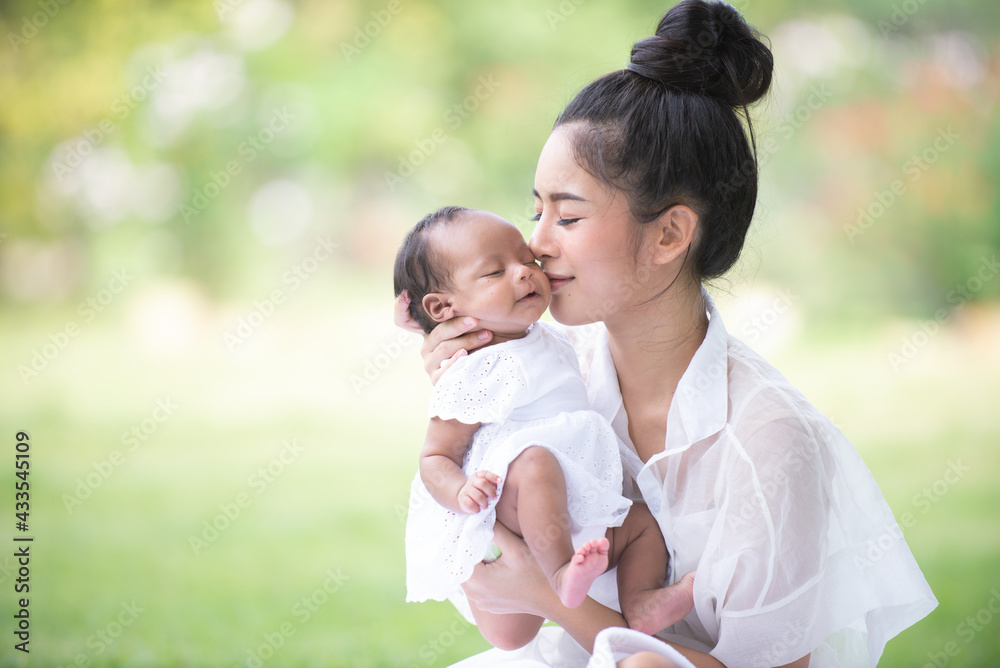 A healthy Asian woman mother, raising a baby in a green garden atmosphere, having a good environment, giving love and warmth.