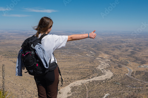 the young girl standing from  the hill hitchhiking over the background of the  desert road