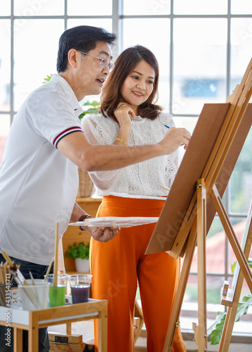 Senior man and woman couple, husband and wife, painting image together in home gallery with warm and happy circumstance. Idea for time-sharing and relaxing for older people after retirement