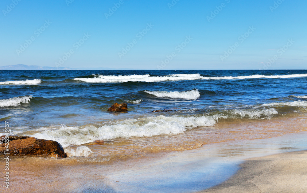 Baikal Lake in summer. Beautiful landscape with waves on the sandy beach of the Barguzinsky Bay on a sunny windy day. Summer holidays and travel. Natural seaside background