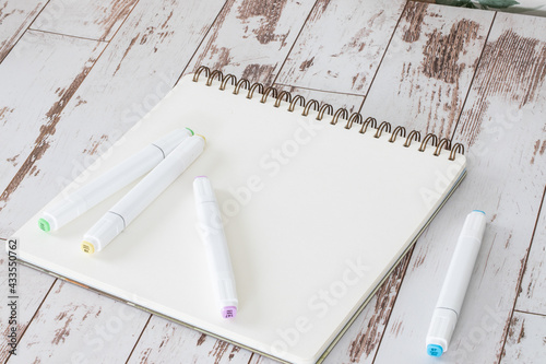 Crayon de couleurs à double pointe déposés sur une feuille de papier blanche vide avec reliure en spirale sur surface de bois