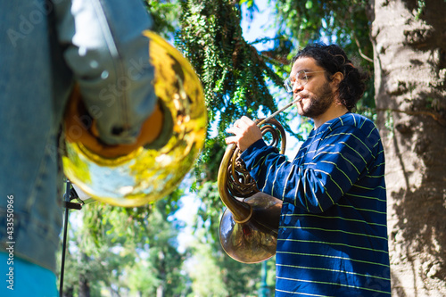 Sticker latin man playing the french horn in a park rehearsing with his band