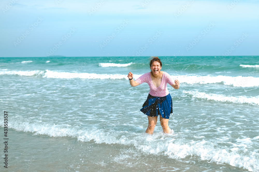 Young Asian woman in a swimsuit is playing water at the beach.