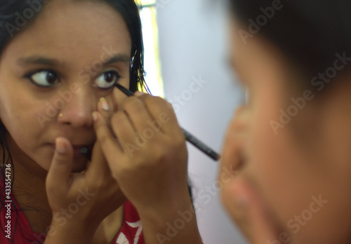 Happy young attractive woman holding brush applying mascara on eyelashes getting ready.