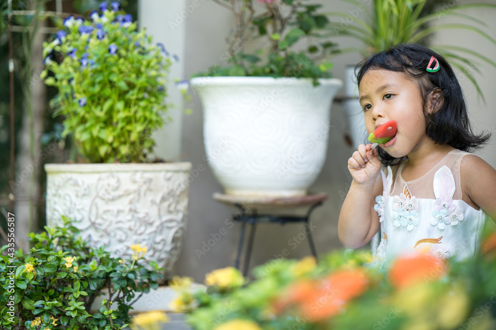 Little asian girl eating ice pop at garden.