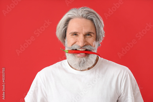 Senior man with chili pepper on color background