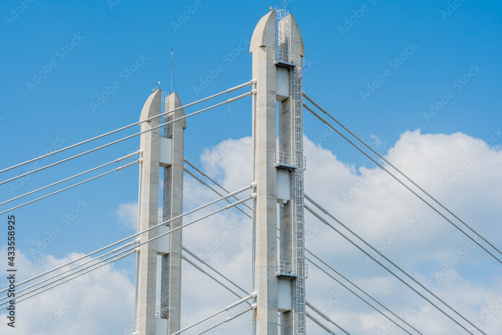 Two concrete columns of cable stay bridge against cloudy blue sky.