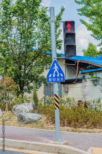 Red crossing light above blue sign with Korean word that says "Crosswalk" in residential neighborhood.