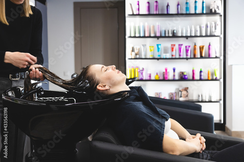 Master woman hairdresser gently washes the girl's hair with shampoo and conditioner before styling in a beauty salon.