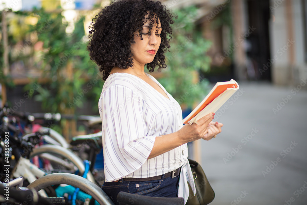Black adult woman reading story book in downtown city. Black adult woman reading story book in downtown city.