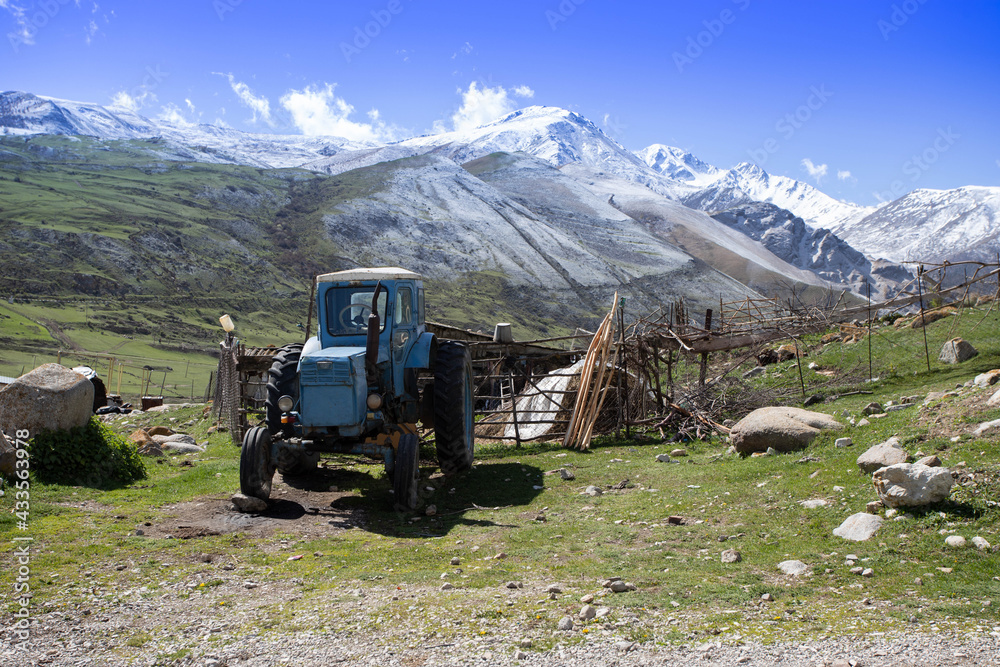 old blue tractor in the village on the background of snowy mountains