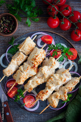 Chicken skewers on wooden skewers with vegetables on a ceramic plate, selective focus