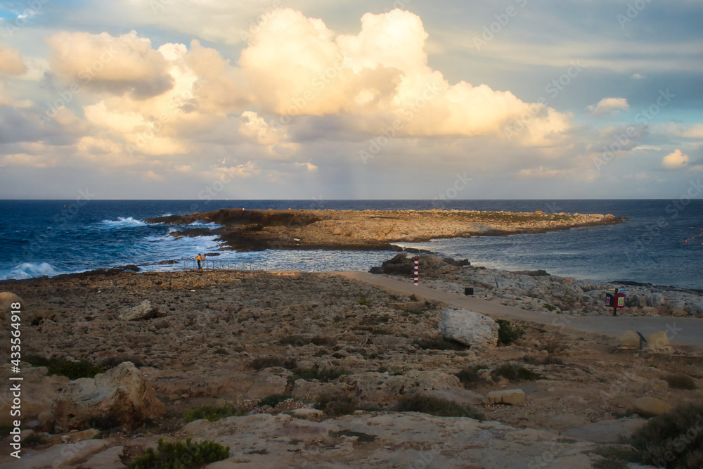 Light shining on small island in the ocean at a beach in Qawra, Malta at sunset.