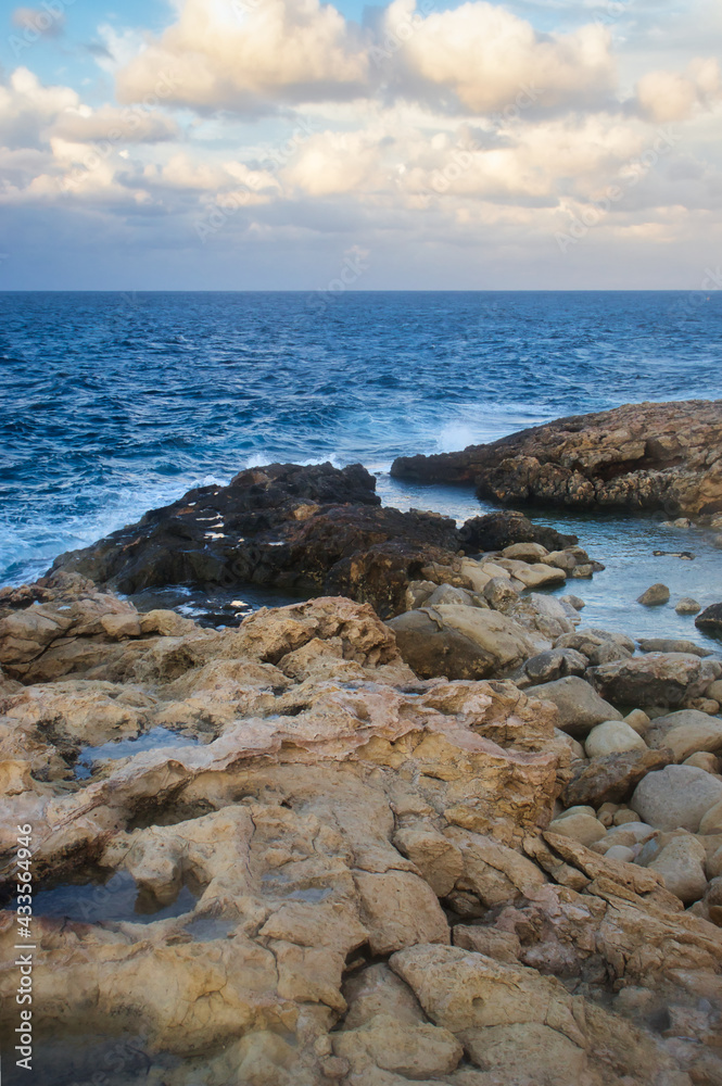 Rocks with pools of water leading out into the blue ocean on a fall evening in Qawra, Malta