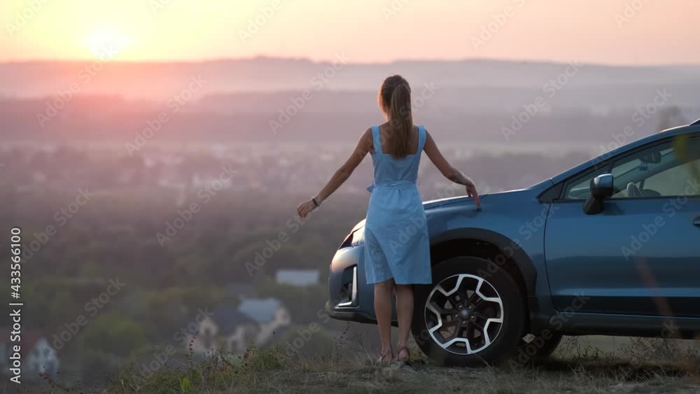 Young female driver resting near her car raising up her hands on warm summer evening. Travel destinations concept. Young female driver resting near her car raising up her hands on warm summer evening. Travel destinations concept.