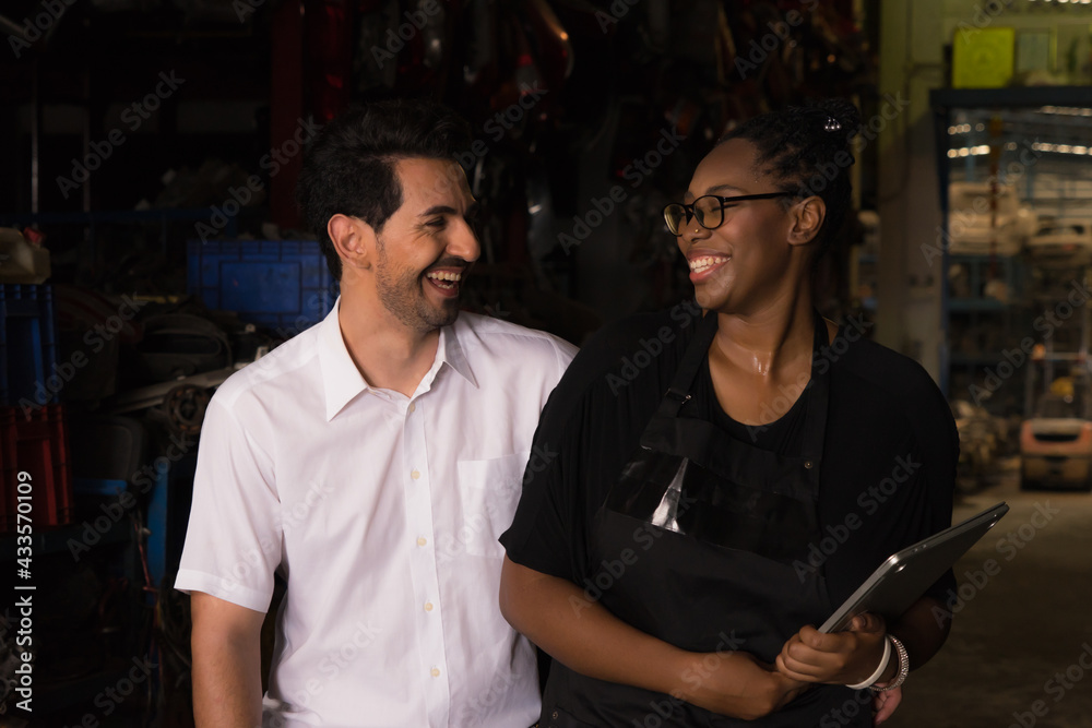 Man work with woman, happy and smiling together. Diversity of two people, caucasian business manager and black African worker woman happy and smiling together in factory-warehouse Man work with woman, happy and smiling together. Diversity of two people, caucasian business manager and black African worker woman happy and smiling together in factory-warehouse