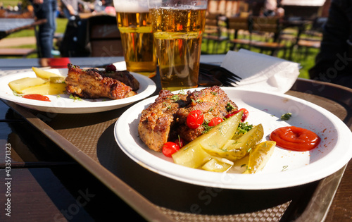 Pork ribs on a tray and light beer on wooden table background. Street food. Festival food on a sunny day