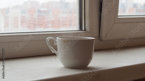 Close up white coffee cup with on the windowsill. pours coffee near window with light shade 