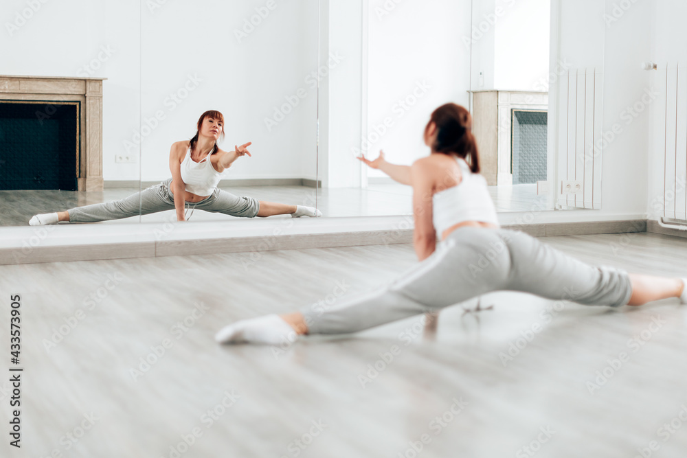 professional female dancer practicing the splits in front of a big mirror in dance school. professional female dancer practicing the splits in front of a big mirror in dance school.