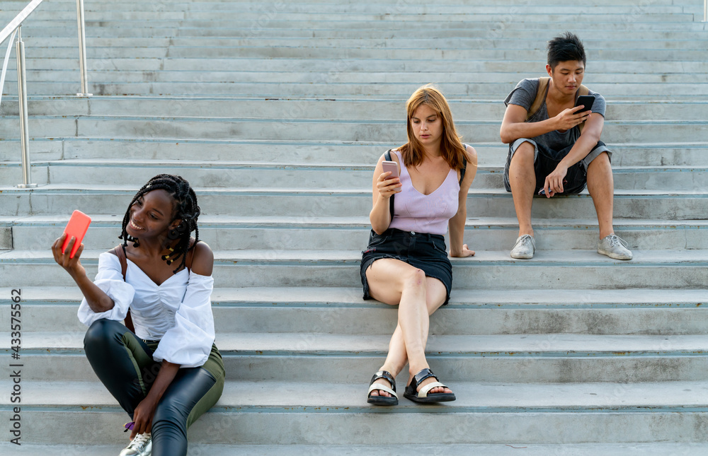 Fototapeta premium Friends checking mobile phones sitting on stairs