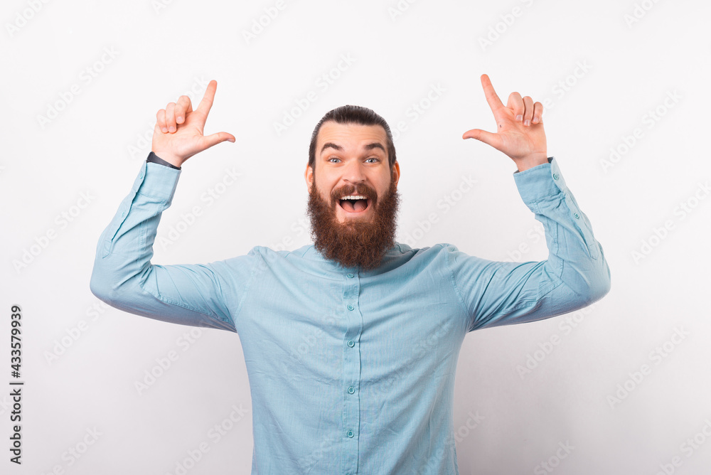 Photo of handsome man with beard in blue shirt pointing up at copyspace Photo of handsome man with beard in blue shirt pointing up at copyspace