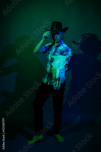 A guy in a cowboy hat and a plaid shirt in a studio with blue and green light