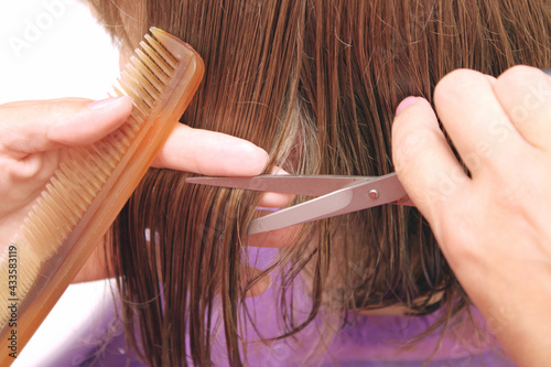 Hand of hairdresser cuts hair of woman close up in beauty salon.