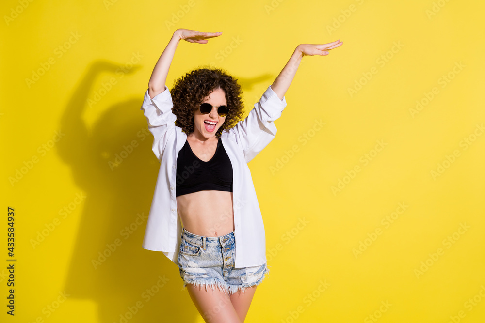 Photo of young happy excited crazy positive funky girl in sunglasses raising hands up in air isolated on yellow color background Photo of young happy excited crazy positive funky girl in sunglasses raising hands up in air isolated on yellow color background