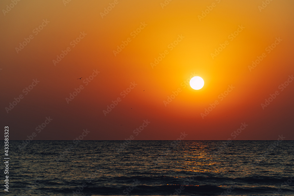 Scenic view of Sun setting in vibrant orange sky reflecting on the water