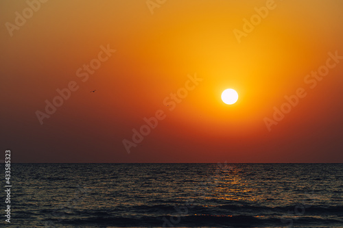Scenic view of Sun setting in vibrant orange sky reflecting on the water © RandomHartz