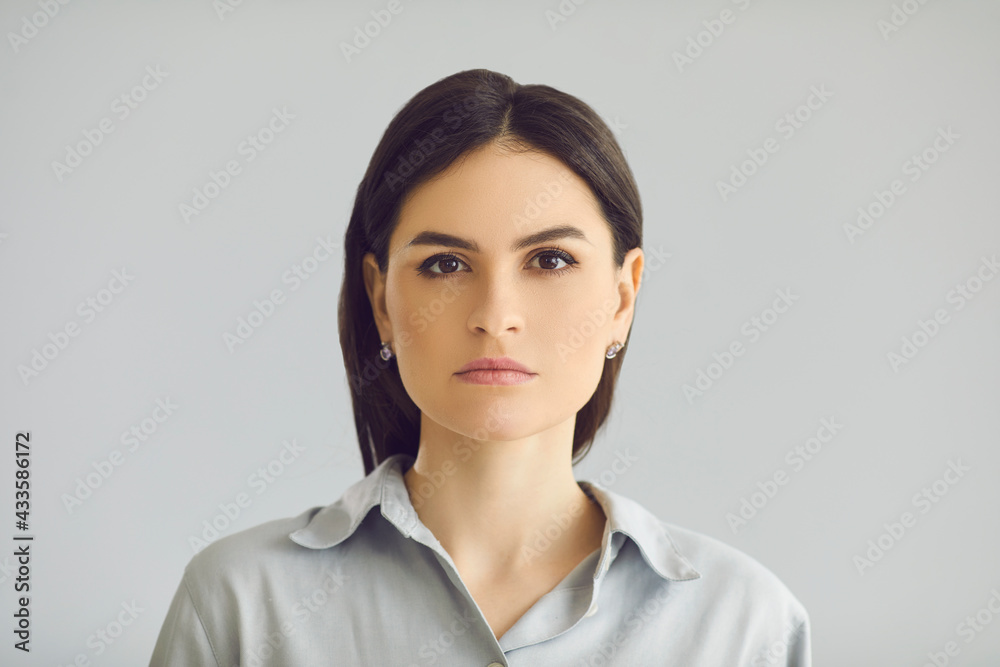 Confident businesswoman, people emotion, youth and beauty. Young calm concentrated thoughtful serious caucasian woman looking at camera face expression portrait on studio grey background Confident businesswoman, people emotion, youth and beauty. Young calm concentrated thoughtful serious caucasian woman looking at camera face expression portrait on studio grey background