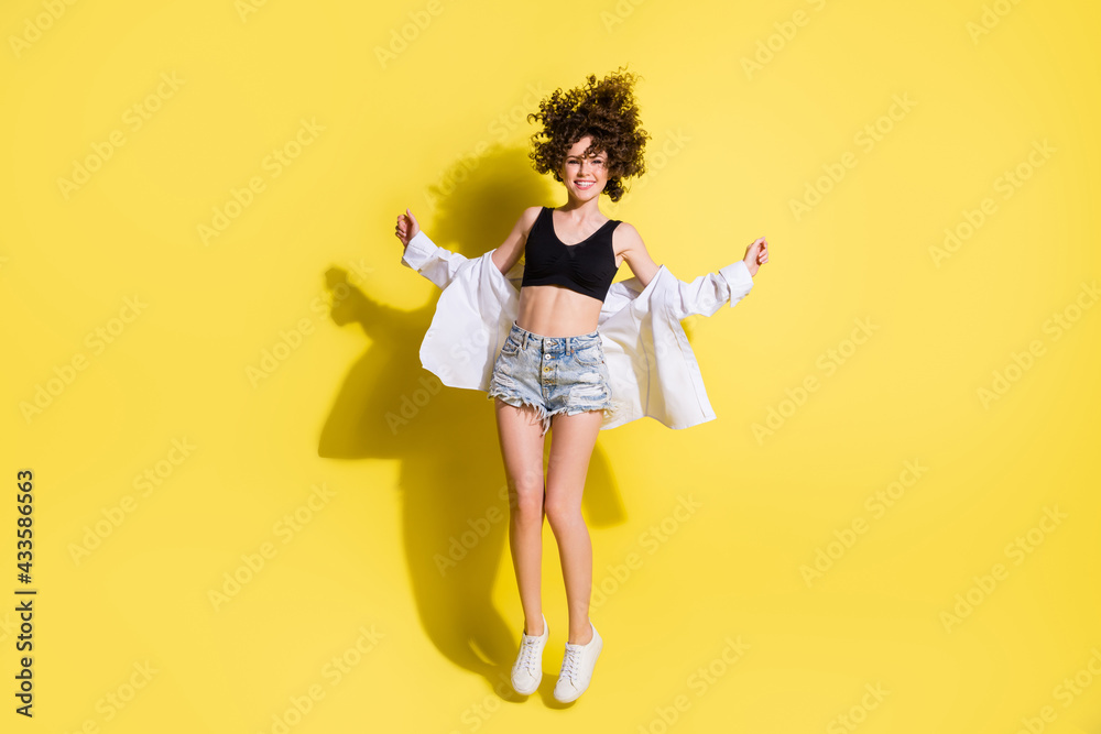 Full size photo of optimistic wavy hairdo girl wear top shorts shirt sneakers isolated on yellow color background Full size photo of optimistic wavy hairdo girl wear top shorts shirt sneakers isolated on yellow color background