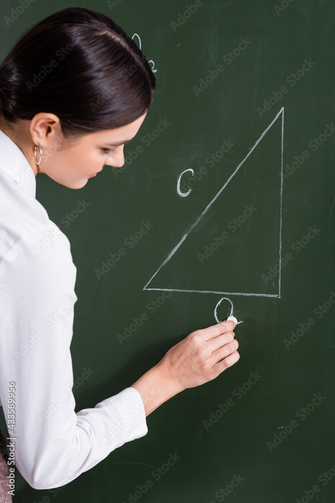 Teacher writing triangle on chalkboard in classroom