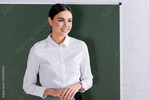 Happy teacher in white shirt standing near chalkboard