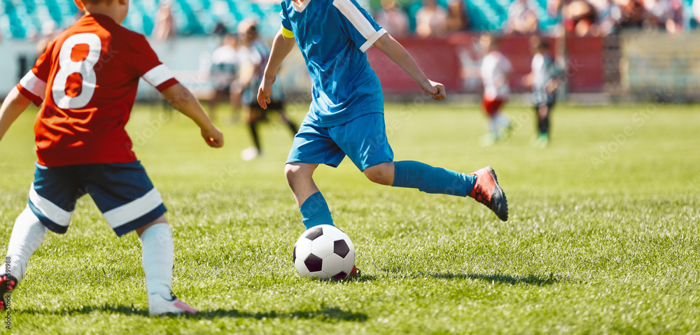 Children playing game on football soccer stadium field. Boys compete during soccer tournament match. Kids in red and blue soccer jersey shirts Children playing game on football soccer stadium field. Boys compete during soccer tournament match. Kids in red and blue soccer jersey shirts