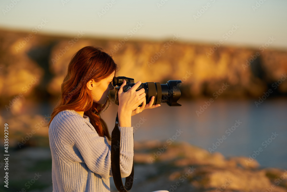 woman with a camera at sunset in the mountains in nature near the sea