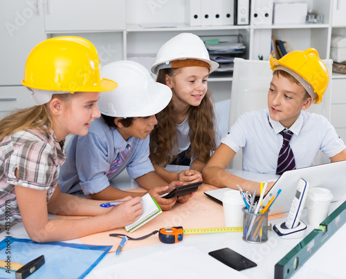 Group of children in helmet talking about building near laptop