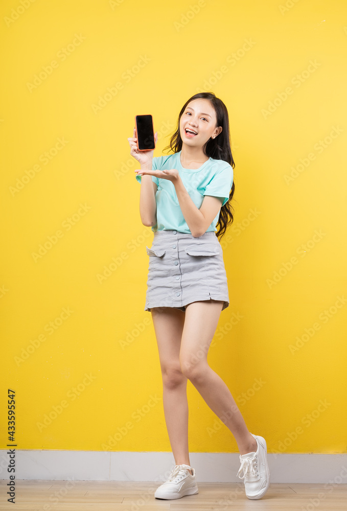 Young Asian girl holding smartphone on yellow background Young Asian girl holding smartphone on yellow background