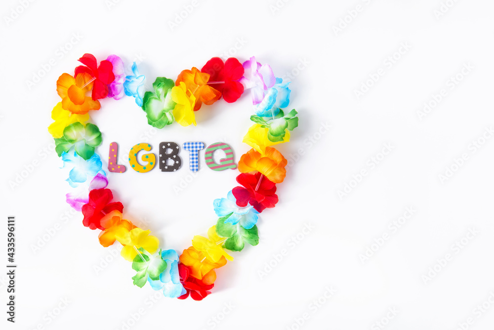 Hawaiian flower necklace in the shape of a heart with LGBTQ inscription inside on the white background. LGBTQ concept with rainbow flag colors. Pride month. Selective focus. Copy space.