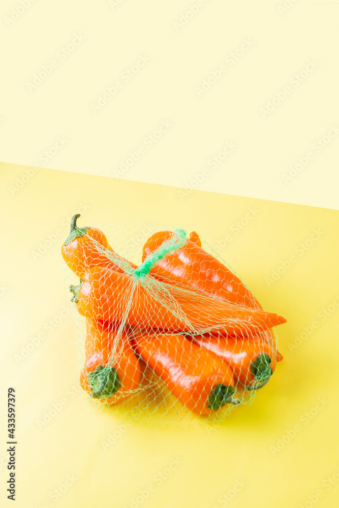 Sweet orange palermo peppers in a string bag on a yellow background. Purchase of fresh vegetables for the vitamin salad. Still life vegetarian minimalistic concept. Organic healthy food