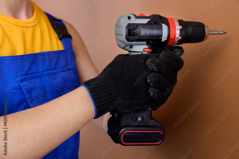 Female hands of a foreman in work gloves holds an electric screwdriver. Studio photography on a brown background Female hands of a foreman in work gloves holds an electric screwdriver. Studio photography on a brown background