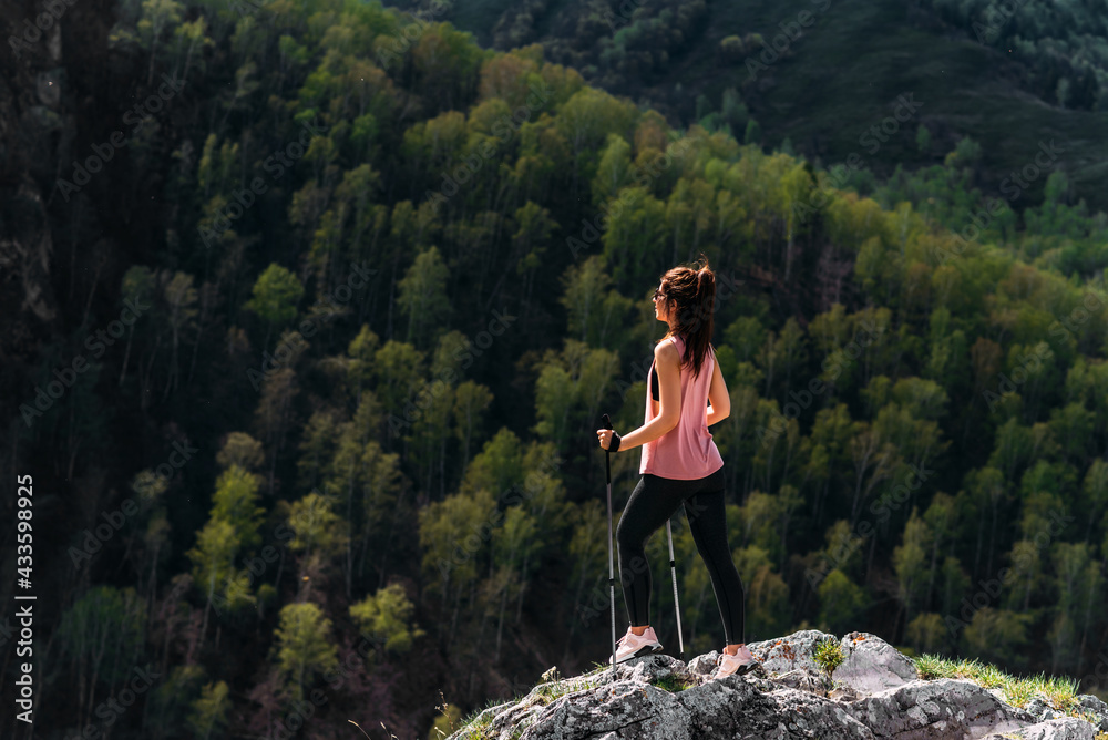 Naklejka premium Hiking in the mountains. A woman is engaged in Nordic walking in the mountains. Tourist in the mountains. A young woman engaged a nordic walking in a mountains. Active leisure time concept. Copy space