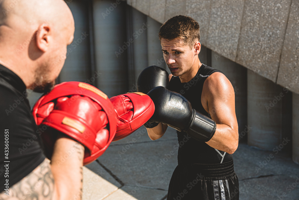 Two men exercising and fighting in outside. Boxer in gloves is training with a coach Two men exercising and fighting in outside. Boxer in gloves is training with a coach