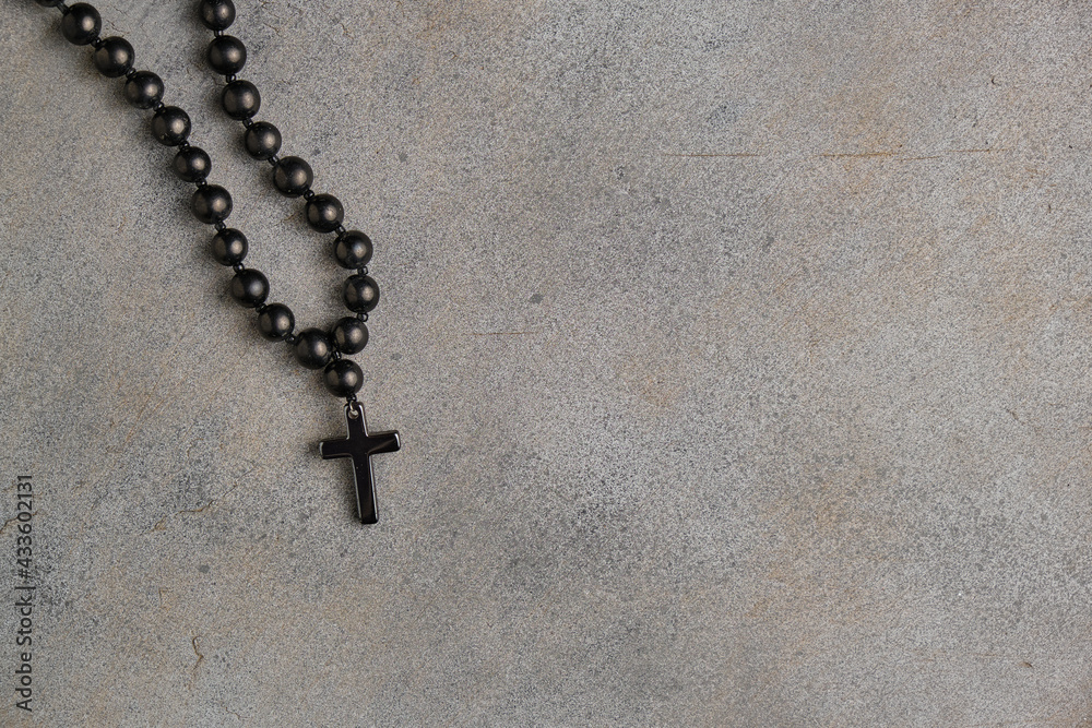 Black obsidian rosary with a cross on an abstract gray background