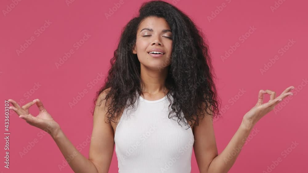 Spiritual young african woman curly hair 20s years old wear white tank top shirt hold spreading hands in yoga om aum gesture relax meditate try to calm down isolated on dark pink color wall background