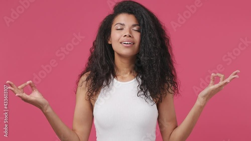 Spiritual young african woman curly hair 20s years old wear white tank top shirt hold spreading hands in yoga om aum gesture relax meditate try to calm down isolated on dark pink color wall background