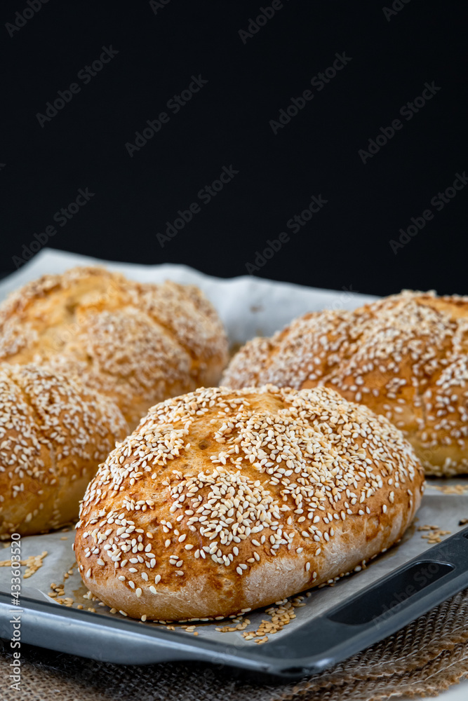 Fresh challah bread rolls hot from the oven on a baking tray. Gluten free bread buns or mini loaves with sesame seeds and golden color ready to eat. Fluffy shaped homemade bread on a dark background.