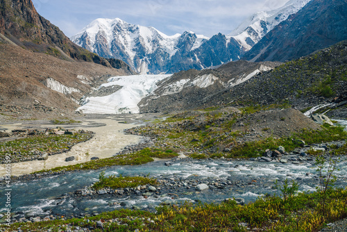 Sunny alpine landscape with confluence of two various mountain rivers on background of snowy mountain with glacier. Beautiful clear creek flows into dirty river. Confluence of two different rivers.