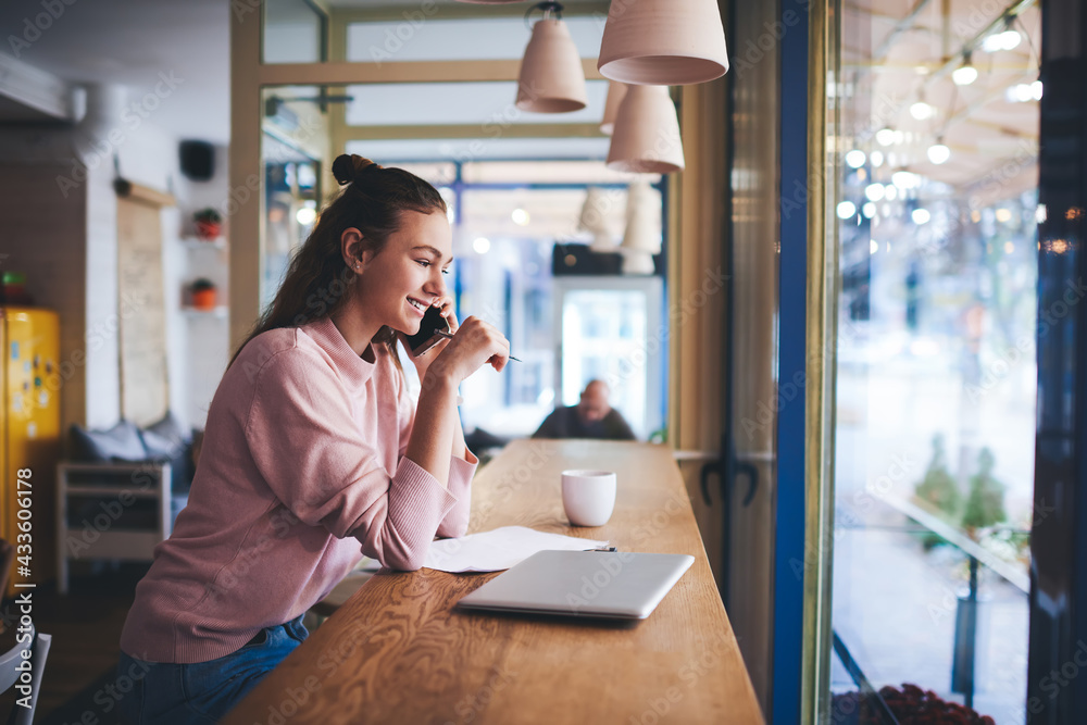 Fototapeta premium Cheerful freelancer speaking on smartphone in cafeteria